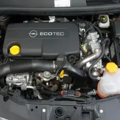 Silnik Opel Corsa D 1.2 benzyna. Widoczny jest czarny dekiel z napisem Ecotec, akumulator Varta oraz zbiornik płynu chłodniczego.