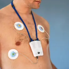 Mężczyzna z przyklejonymi elektrodami do klatki piersiowej i zawieszonym na szyi urządzeniem. To holter, który monitoruje pracę serca.