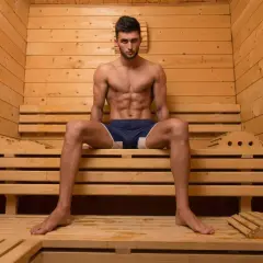 Mężczyzna z wyrzeźbionym brzuchem relaksuje się w drewnianej saunie po treningu.