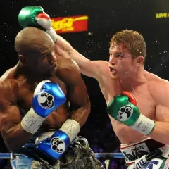 Two boxers exchange blows, one with a blue boxing guard, the other with a green one. Sweat flies as they fight.