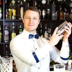 Uśmiechnięty barman z shakerem w dłoniach, za nim półki z alkoholem. Zastanawiasz się, ile zarabia barman za granicą?
