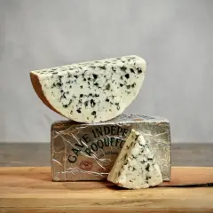 Un morceau de roquefort est posé sur son emballage argenté, avec une autre part en triangle à côté.