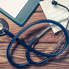 Stetoscopio, penna, cartella e mascherina su tavolo di legno. Preparativi per aprire studio medico in appartamento.