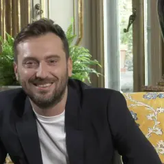 Un uomo sorride, con un blazer scuro e una maglietta bianca. I testi di Cesare Cremonini dicono di me che sono felice.