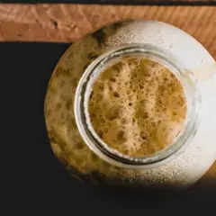 Ein Glas mit schaumigem Sauerteig, der aussieht wie kleine Flocken im Bier.