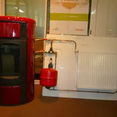 Poêle à granulé hydro rouge connecté à un radiateur blanc. Le système de chauffage est prêt.