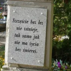 Kamienna płyta z napisem "Szczęście bez łez nie istnieje, tak samo jak nie ma życia bez śmierci". W tle cmentarz, kwiaty i znicze. Prochy po kremacji spoczywają w tym miejscu.