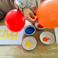 Kinder malen mit Luftballons bunte Muster auf Papier. Rote und orange Luftballons werden in Farbe getaucht.