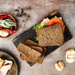 Pyszny chleb z razowej mąki pszennej, idealny na kanapki. Obok składniki: pomidor, ser, wędlina, czosnek, papryczki chili i zioła.