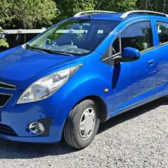 Blå Chevrolet Spark med extraljus, kanske ett problem med bilen? Parkerad på grusväg.