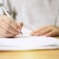 Dłoń pisze długopisem na dokumencie. Umowa najmu na czas określony przechodzi na czas nieokreślony.