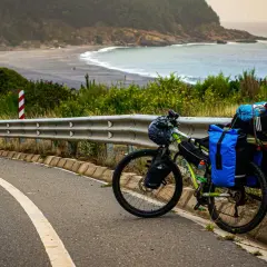 Rower MTB gotowy do bikepackingu, zapakowany przy drodze z widokiem na ocean i plażę.