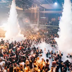 Folla in delirio in una discoteca, tra fumo e luci. Un'atmosfera elettrizzante che fa pensare alle migliori discoteche Madrid.