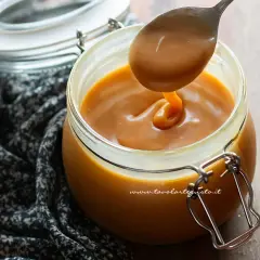 Un cucchiaio raccoglie un denso caramello salato da un barattolo di vetro.