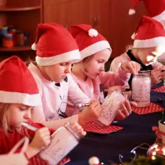 Dzieci w mikołajkowych czapkach tworzą świąteczne słoiki. 6 grudnia to idealny czas na takie kreatywne zabawy.