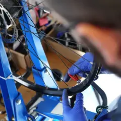 Ręce w niebieskich rękawiczkach dokonują centrowania koła rowerowego za pomocą klucza.