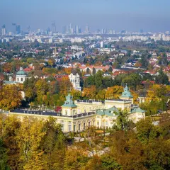 Pałac wilanowski otoczony jesiennym parkiem, z panoramą Warszawy w tle. To symbol najbogatszej dzielnicy Warszawy.