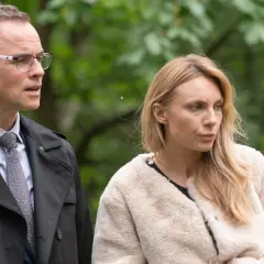 Adam i Ewa obsada: mężczyzna w okularach i płaszczu oraz kobieta w futrzanej kurtce na tle zieleni.