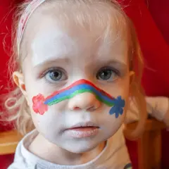 Ein kleines Mädchen mit einem Regenbogen im Gesicht und Blumen auf den Wangen. Kinderschminken einfach gemacht!