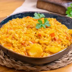 Un plato humeante de arroz con bacalao, adornado con perejil fresco, servido en un cuenco azul sobre una esterilla de mimbre.