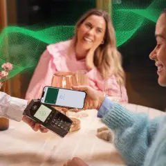 Uśmiechnięte kobiety płacą telefonem w restauracji. Pozytywne fortum opinie o szybkich płatnościach.