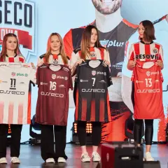 Cztery młode kobiety prezentują koszulki siatkarskie drużyny Asseco Resovia. Dwie w białych, dwie w ciemnych strojach.