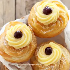 Tre zeppole fritte napoletane, dorate e spolverate di zucchero a velo, con crema pasticcera e una ciliegina.