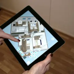 Mit einem Tablet wird die Planung zum Haus einrichten. Eine Person navigiert durch einen 3D-Grundriss, um Möbel zu platzieren und Räume zu gestalten.
