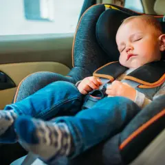 Małe dziecko śpi w foteliku samochodowym, jego opadająca głowa w foteliku świadczy o głębokim śnie podczas podróży.
