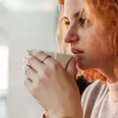 Ruda kobieta pije kawę, czując jak 1000 mg kofeiny na raz pobudza jej zmysły.