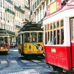 Żółty i czerwony tramwaj w Lizbonie pędzą wąską uliczką między zabytkowymi kamienicami.