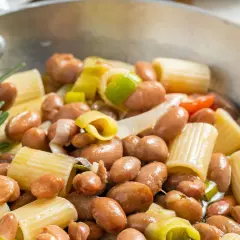 Minestra di fagioli con pasta rigata, cipollotto e rosmarino in una padella.