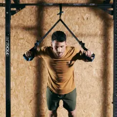 Mężczyzna wykonuje ćwiczenia TRX, trzymając uchwyty taśm treningowych.