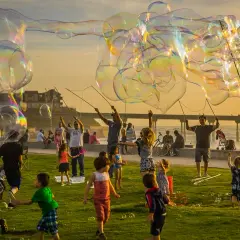 Un compleanno alternativo per bambini con bolle giganti al tramonto. Bambini e adulti si divertono a creare enormi bolle iridescenti sulla costa.