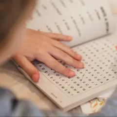 Mano de niño resolviendo una sopa de letras para la memoria con un lápiz naranja.