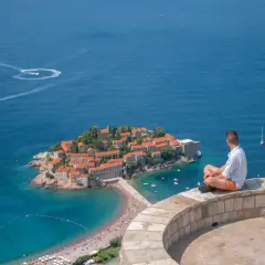 Mężczyzna siedzi na murze, podziwiając wyspę Sveti Stefan. Czy Czarnogóra jest bezpieczna? Tak, to spokojne miejsce na wakacje.