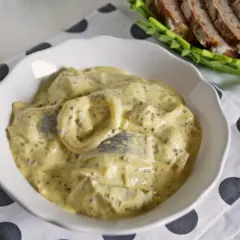 Śledzie z musztardą francuską i czerwona cebula w kremowym sosie, podane z chlebem żytnim.