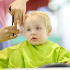 Mały chłopiec z blond włosami otrzymuje swoją pierwszą fryzurę. Włosy są delikatnie cięte, tworząc urocze fryzury dla rocznego chłopca.
