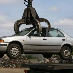 Un'auto d'argento viene sollevata da una gru, pronta per la rottamazione. Un'opportunità per un bonus rottamazione auto senza acquisto.
