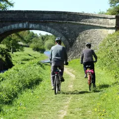 Dwie osoby na rowerach pod kamiennym mostem. Piękna pogoda sprzyja odkrywaniu tras rowerowych lubuskich.