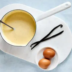 Zutaten für vanillesauce selber machen: ein Topf mit cremiger Sauce, zwei Eier und zwei Vanilleschoten.