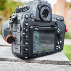 Nikon D850 test w plenerze. Aparat leży na drewnianym stole, w tle zieleń i budynek.