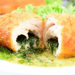 Kotlet de volaille przekrojony na pół, z widocznym nadzieniem z ziół i masła, na talerzu z koperkiem.