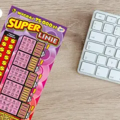 Zdrapka "Super Linie" z symbolami dolara i ikonkami, obok klawiatury i słuchawek.