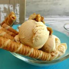 Delicioso helado de dulce de leche con barquillos crujientes y nueces, servido en un cuenco de vidrio sobre un plato turquesa.