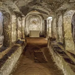 Corridoio sotterraneo con sedute in pietra e affreschi sbiaditi, parte dell'antico borgo di Sutri.
