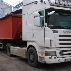 Biała Scania R420 z naczepą "Handel Opałem" stoi przy silosach. Zastanawiasz się, ile kosztuje nowa Scania?