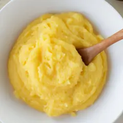 Un tazón blanco lleno de polenta cremosa, con una cuchara de madera. ¿Sabes qué es la polenta? Es un plato reconfortante.