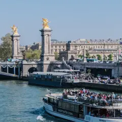 Rejs po Sekwanie w Paryżu. Statek wycieczkowy z turystami płynie w stronę mostu z rzeźbami.