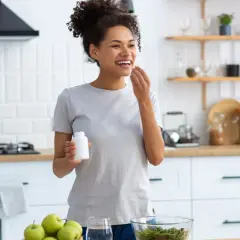 Mujer sonriente en cocina, tomando suplemento. El zinc para que sirve en la mujer es clave para su bienestar general y salud.
